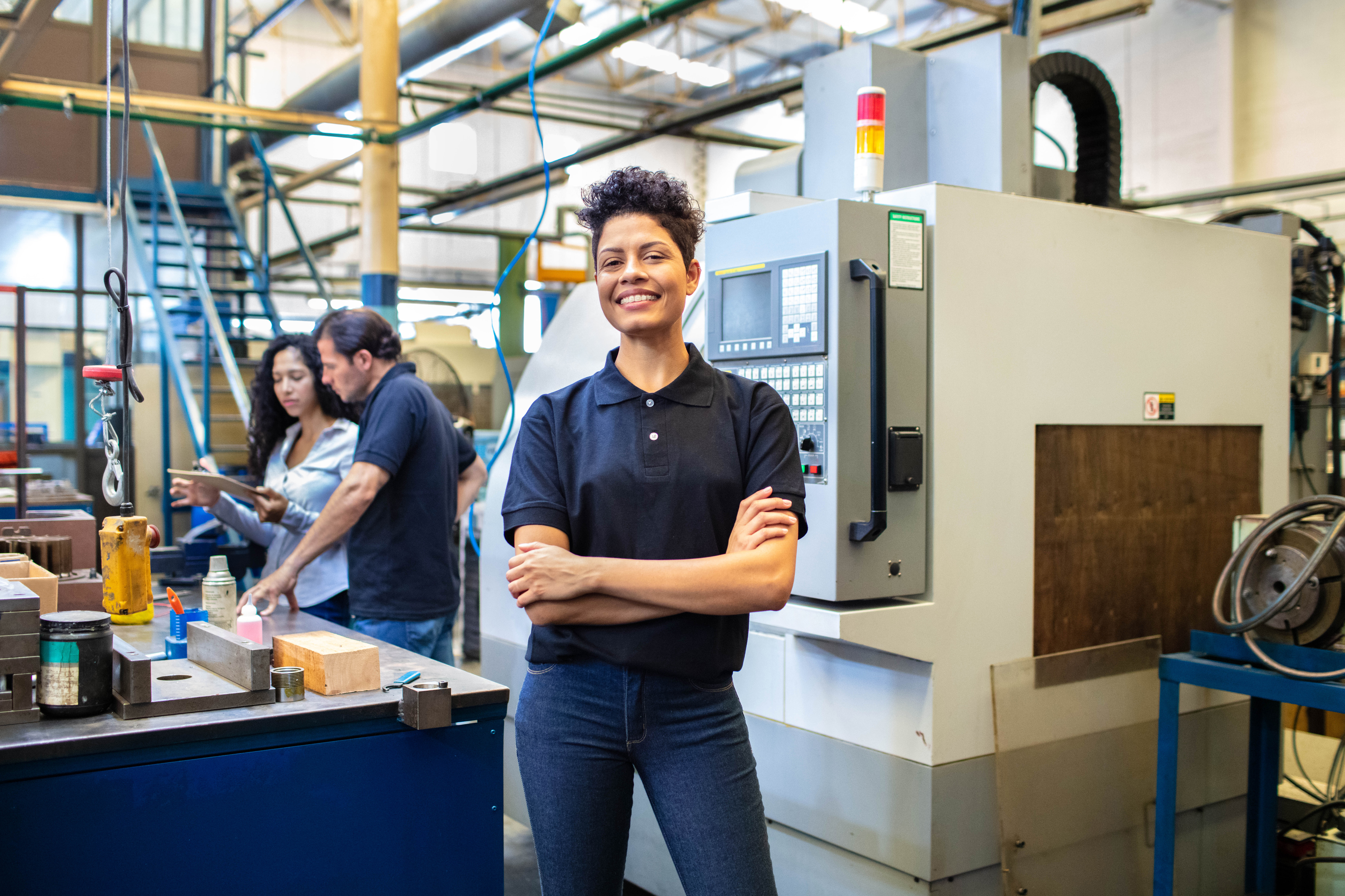 Kvinnlig ingenjör ler mot kameran, ståendes framför maskiner i en fabrik